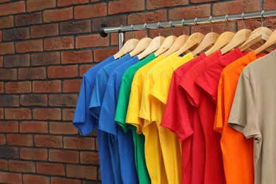 Many colorful t-shirts on clothing rack near brick wall