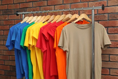 Many colorful t-shirts on clothing rack near brick wall