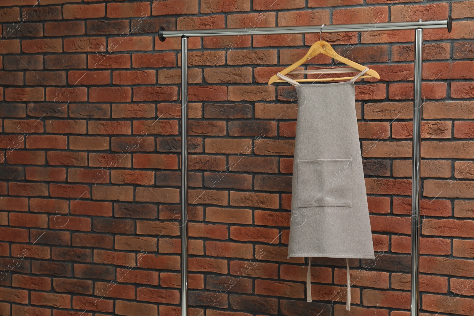 Photo of One chef's apron on clothing rack near brick wall, space for text