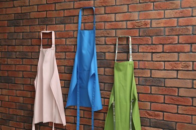 Photo of Many chef's aprons hanging on brick wall