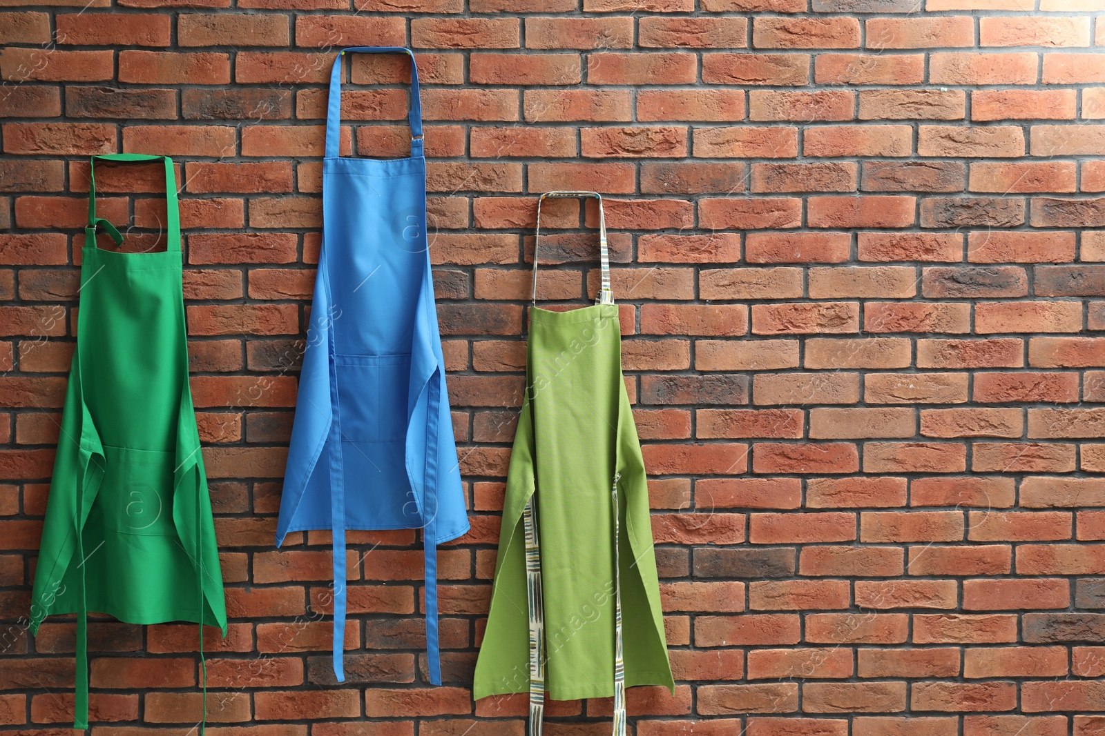 Photo of Many chef's aprons hanging on brick wall, space for text