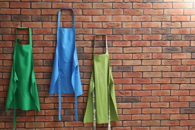 Photo of Many chef's aprons hanging on brick wall, space for text