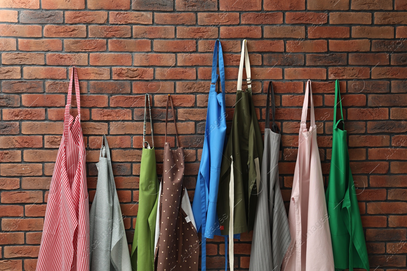 Photo of Many chef's aprons hanging on brick wall