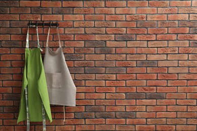 Photo of Two chef's aprons hanging on brick wall, space for text