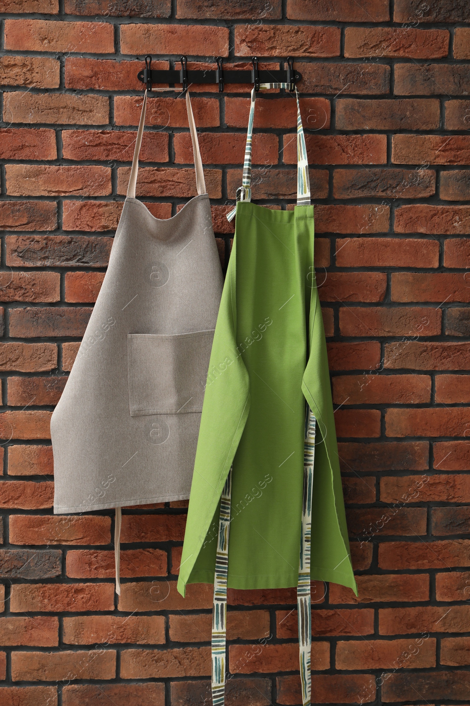 Photo of Two chef's aprons hanging on brick wall