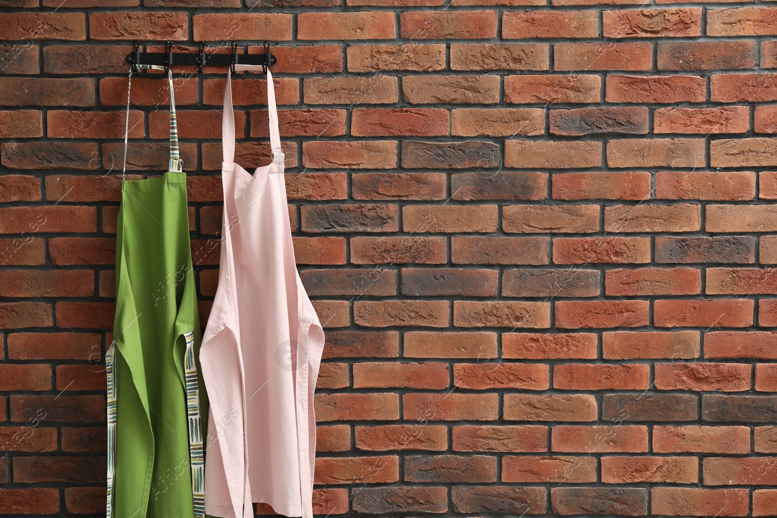 Photo of Two chef's aprons hanging on brick wall, space for text