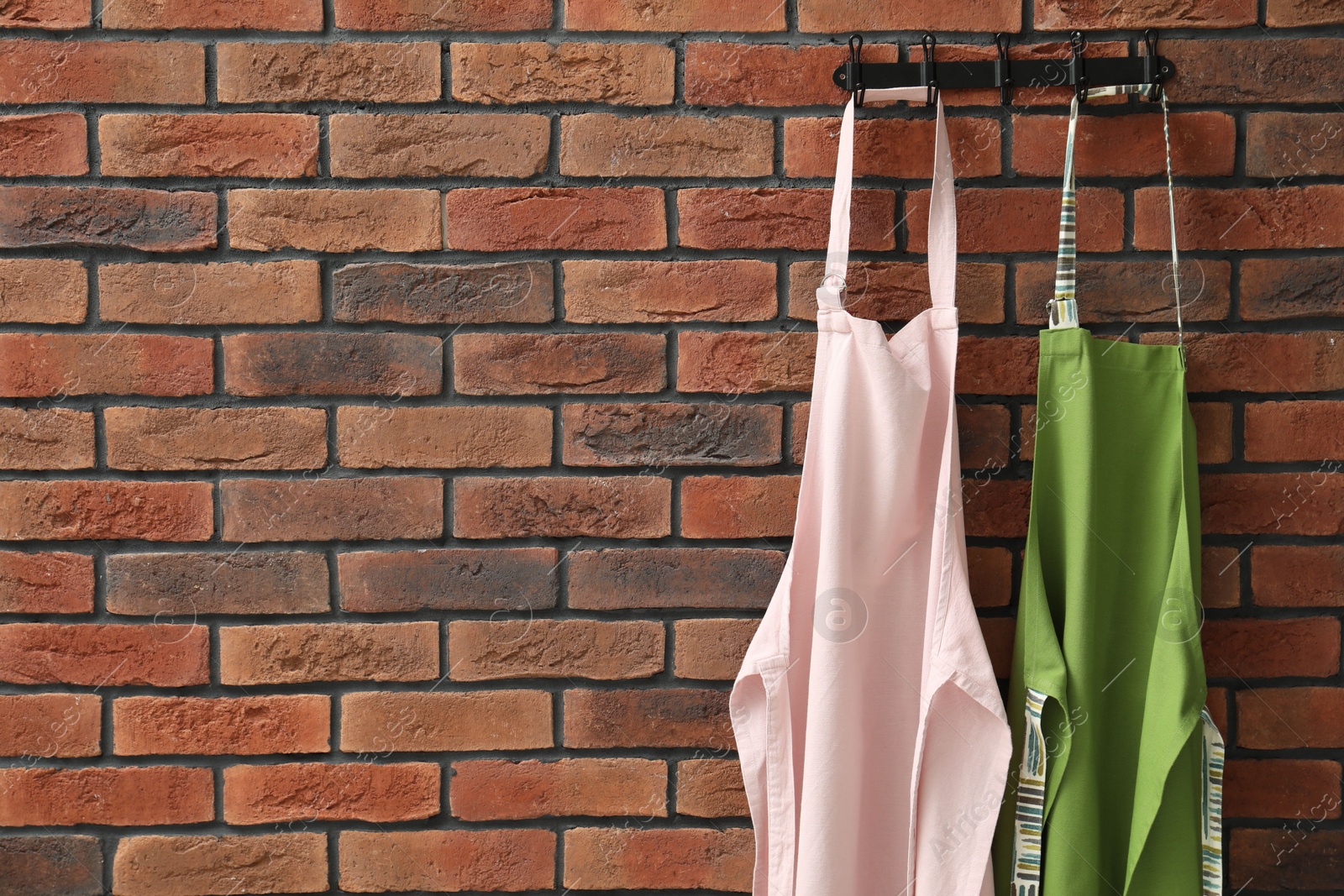 Photo of Two chef's aprons hanging on brick wall, space for text