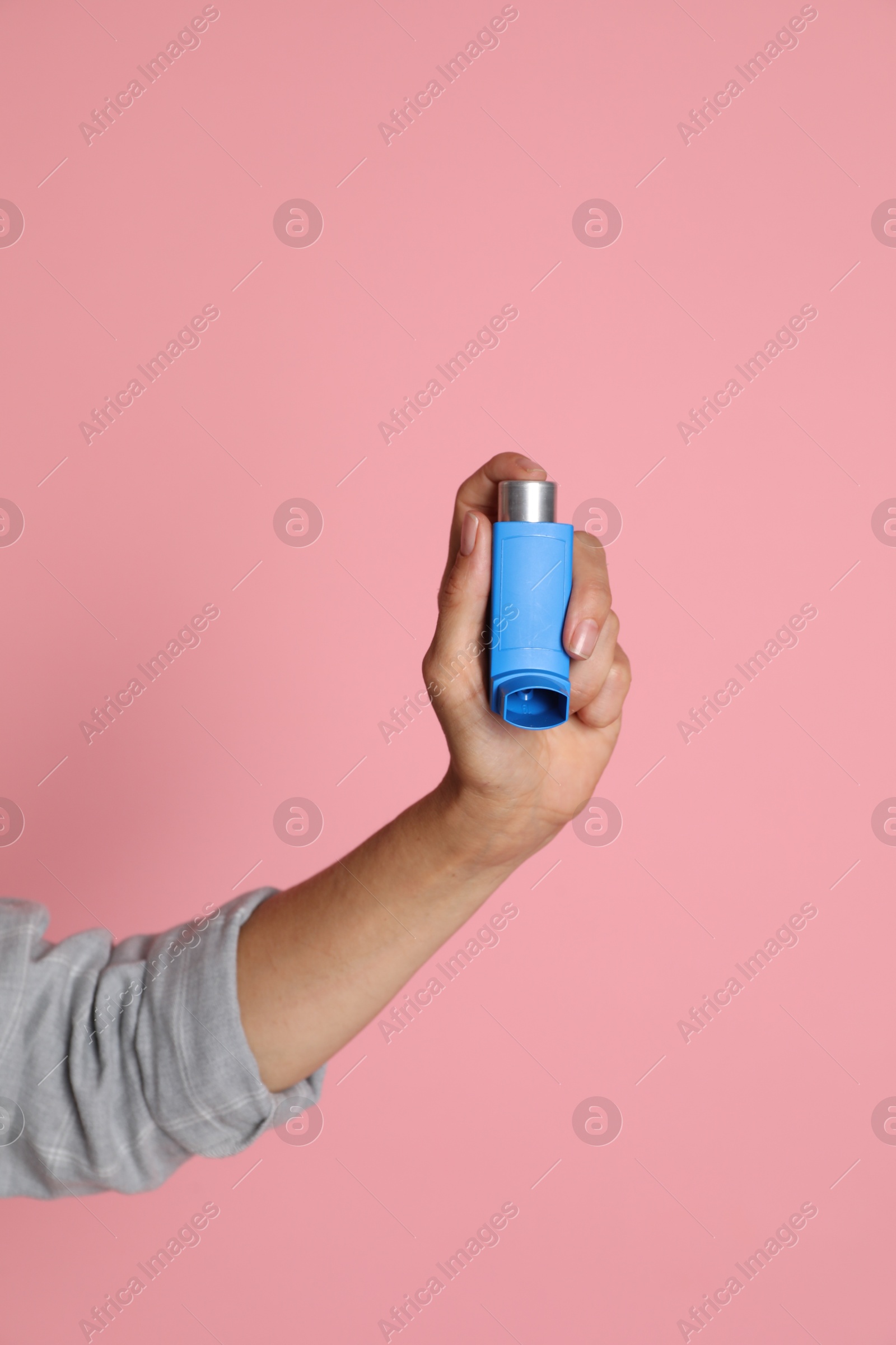 Photo of Woman holding asthma inhaler on pink background, closeup