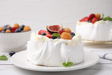 Photo of Pavlova cake (meringue dessert) with whipped cream, fresh berries, fig and mint on white wooden table, closeup