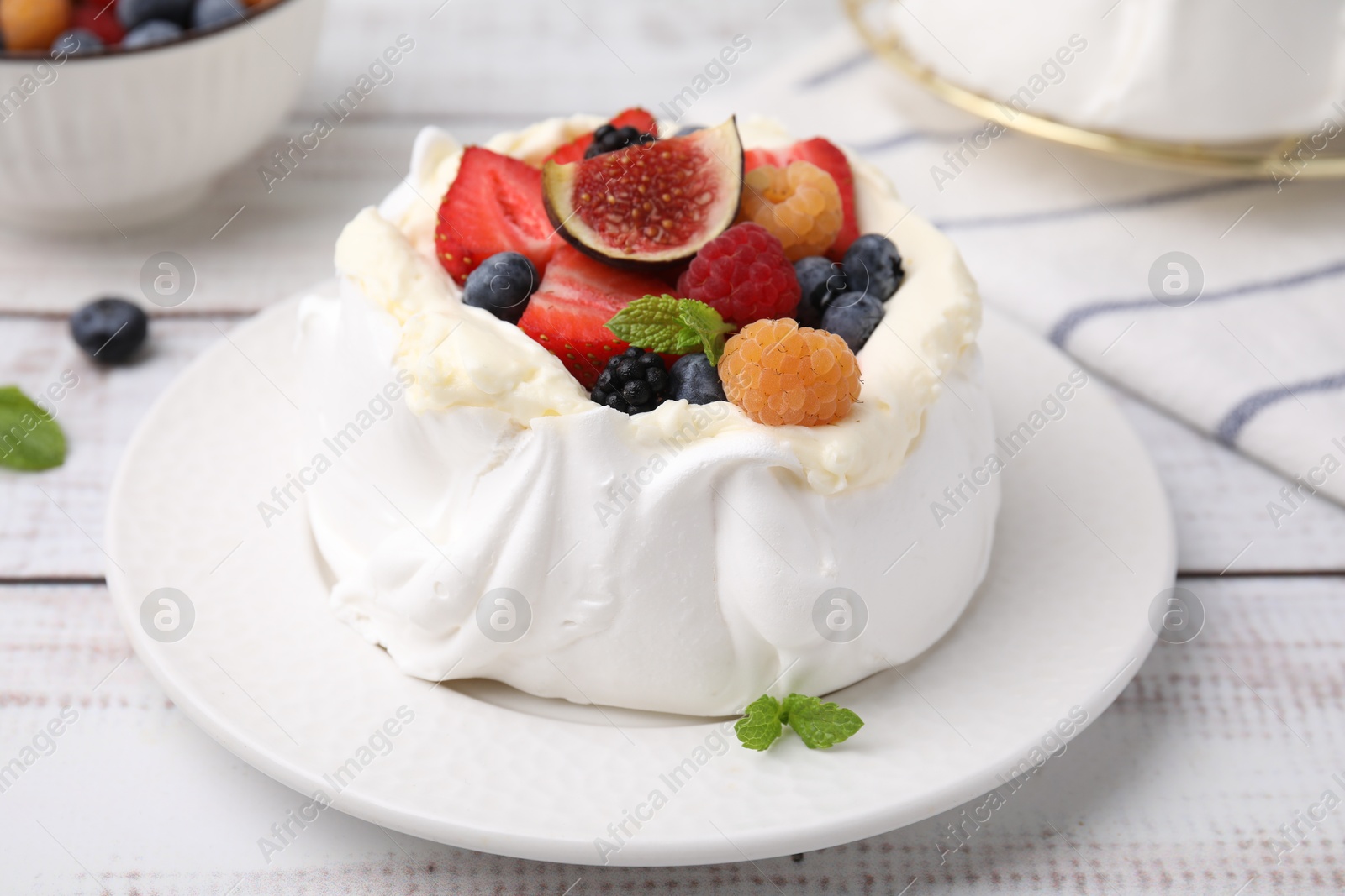 Photo of Pavlova cake (meringue dessert) with whipped cream, fresh berries, fig and mint on white wooden table, closeup