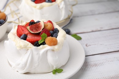 Photo of Pavlova cake (meringue dessert) with whipped cream, fresh berries, fig and mint on white wooden table, closeup