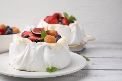 Photo of Pavlova cake (meringue dessert) with whipped cream, fresh berries, fig and mint on white wooden table, closeup