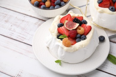 Photo of Pavlova cake (meringue dessert) with whipped cream, fresh berries, fig and mint on white wooden table, closeup