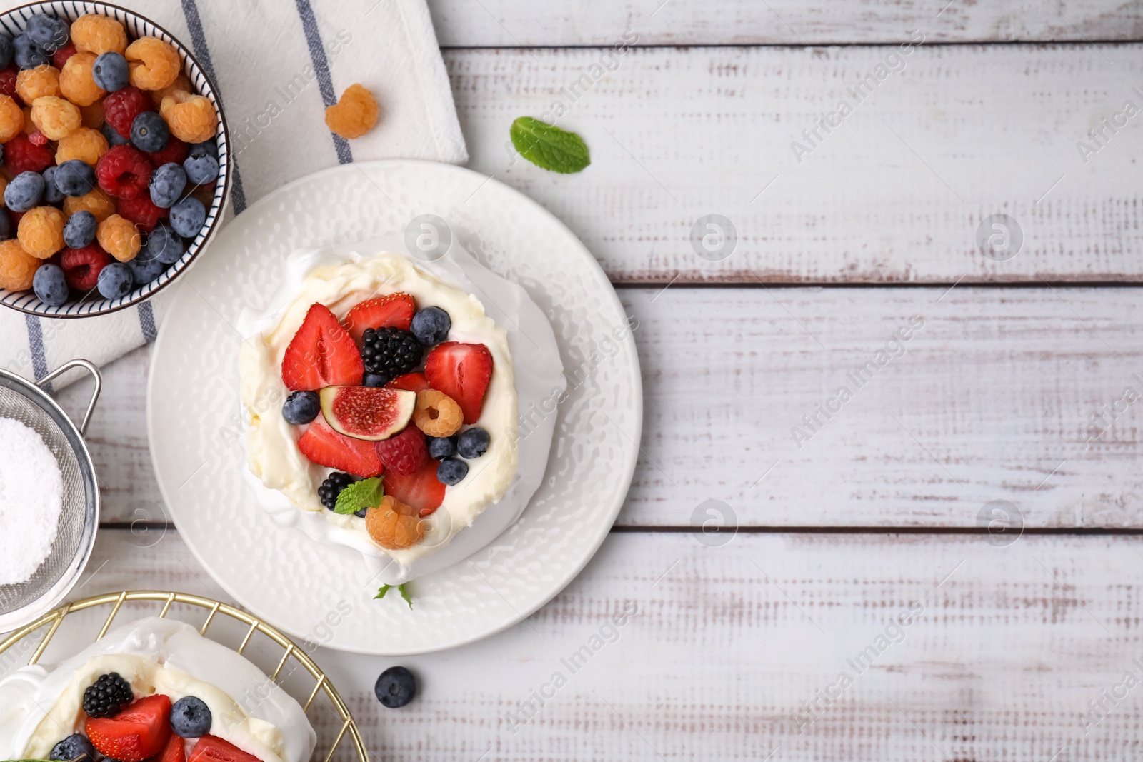 Photo of Pavlova cake (meringue dessert) with whipped cream, fresh berries, fig and mint on white wooden table, flat lay. Space for text