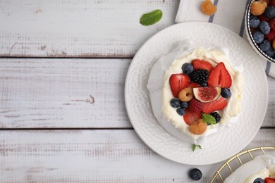 Photo of Pavlova cake (meringue dessert) with whipped cream, fresh berries, fig and mint on white wooden table, flat lay. Space for text