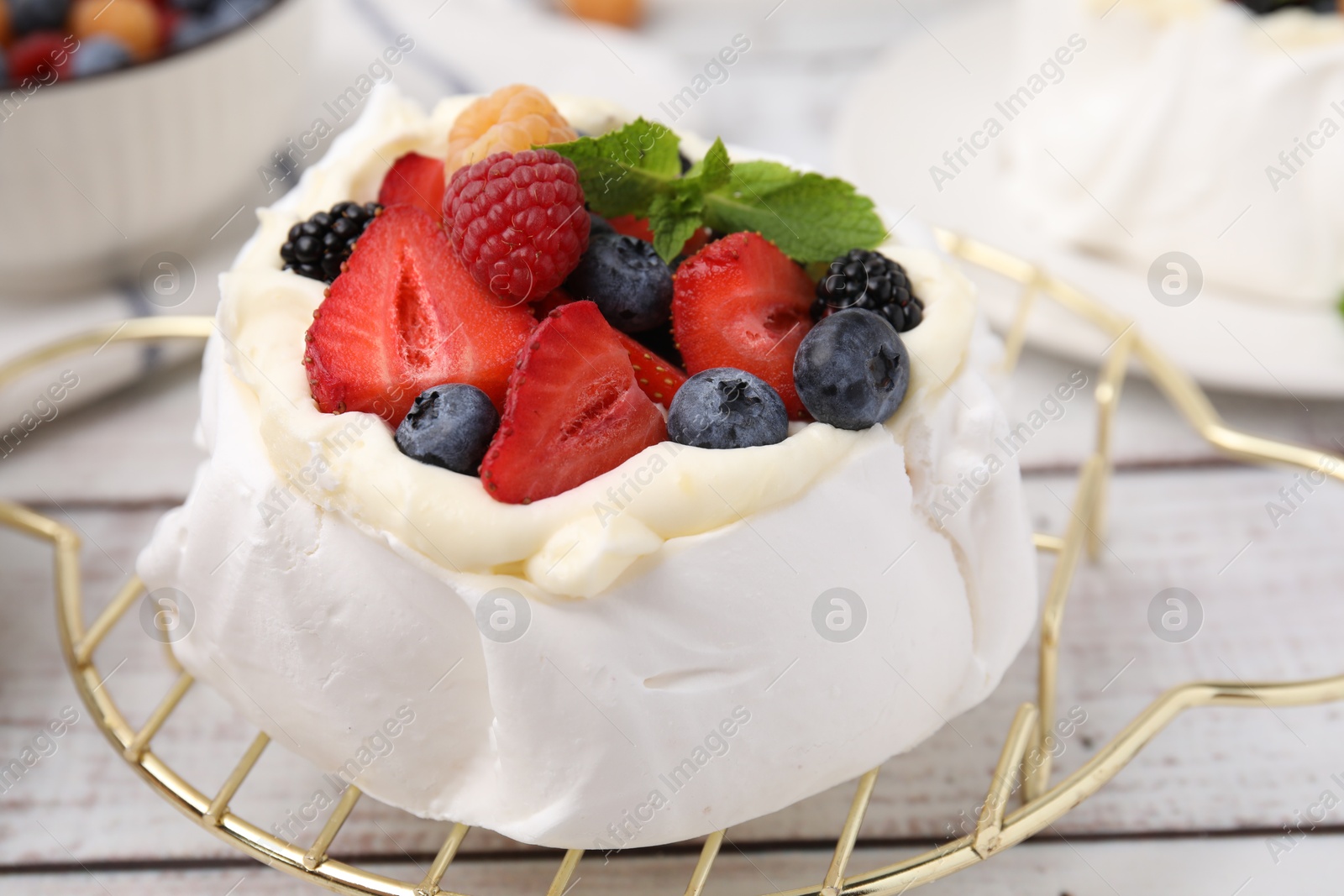 Photo of Pavlova cake (meringue dessert) with whipped cream, fresh berries and mint on white wooden table, closeup