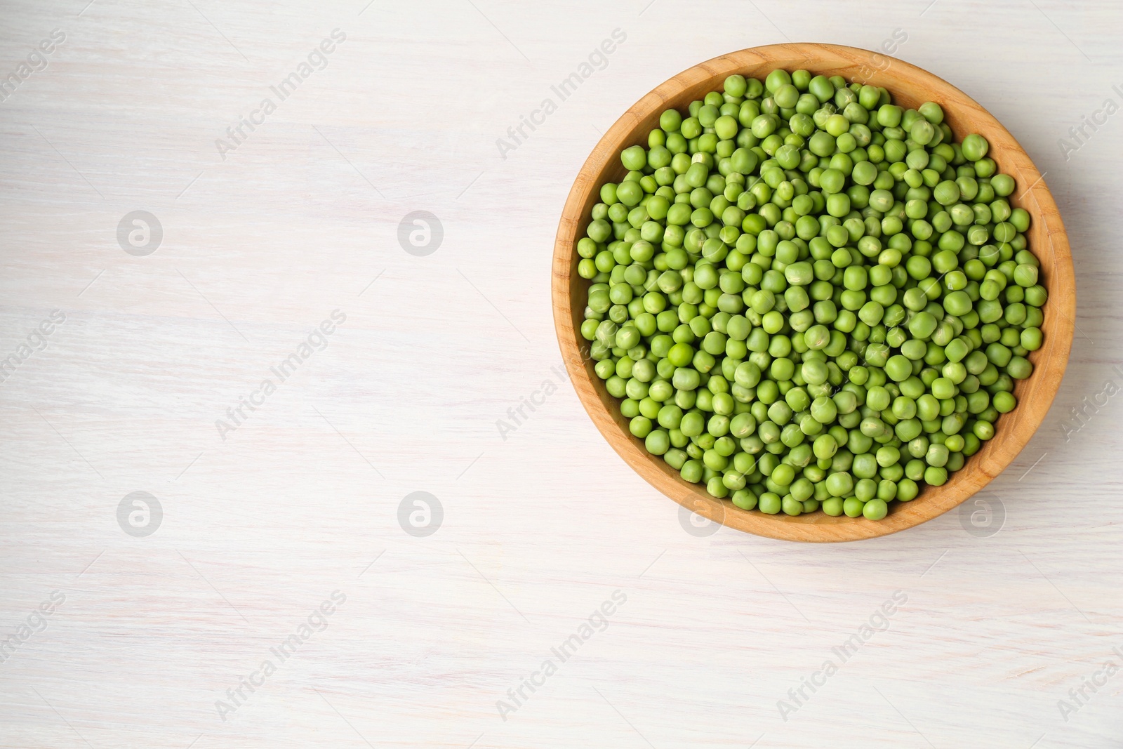 Photo of Fresh green peas in bowl on white wooden table, top view. Space for text