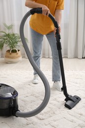 Woman cleaning carpet with vacuum in living room, closeup