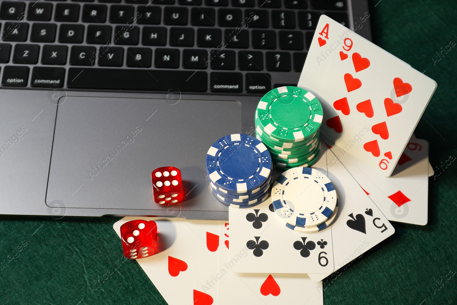 Photo of Poker chips, laptop, playing cards and dices on green table. Online game