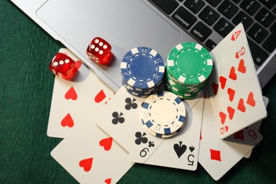 Photo of Poker chips, laptop, playing cards and dices on green table, flat lay. Online game