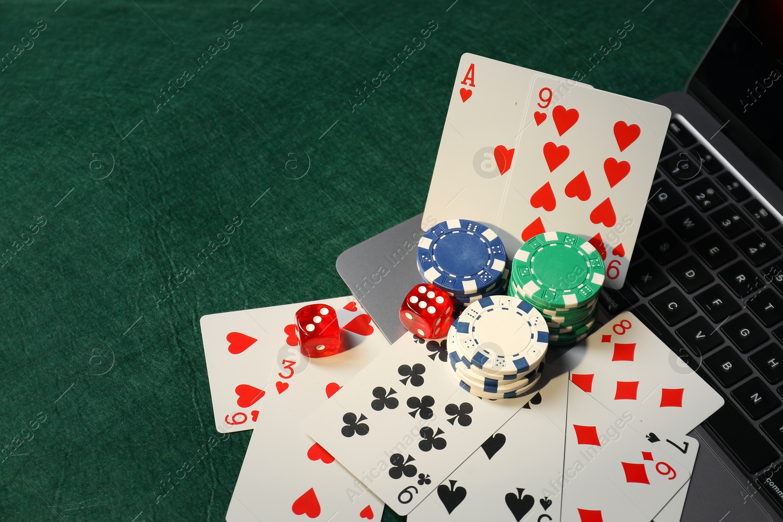 Photo of Poker chips, laptop, playing cards and dices on green table. Online game