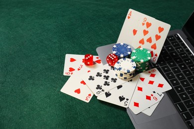 Photo of Poker chips, laptop, playing cards and dices on green table, space for text. Online game