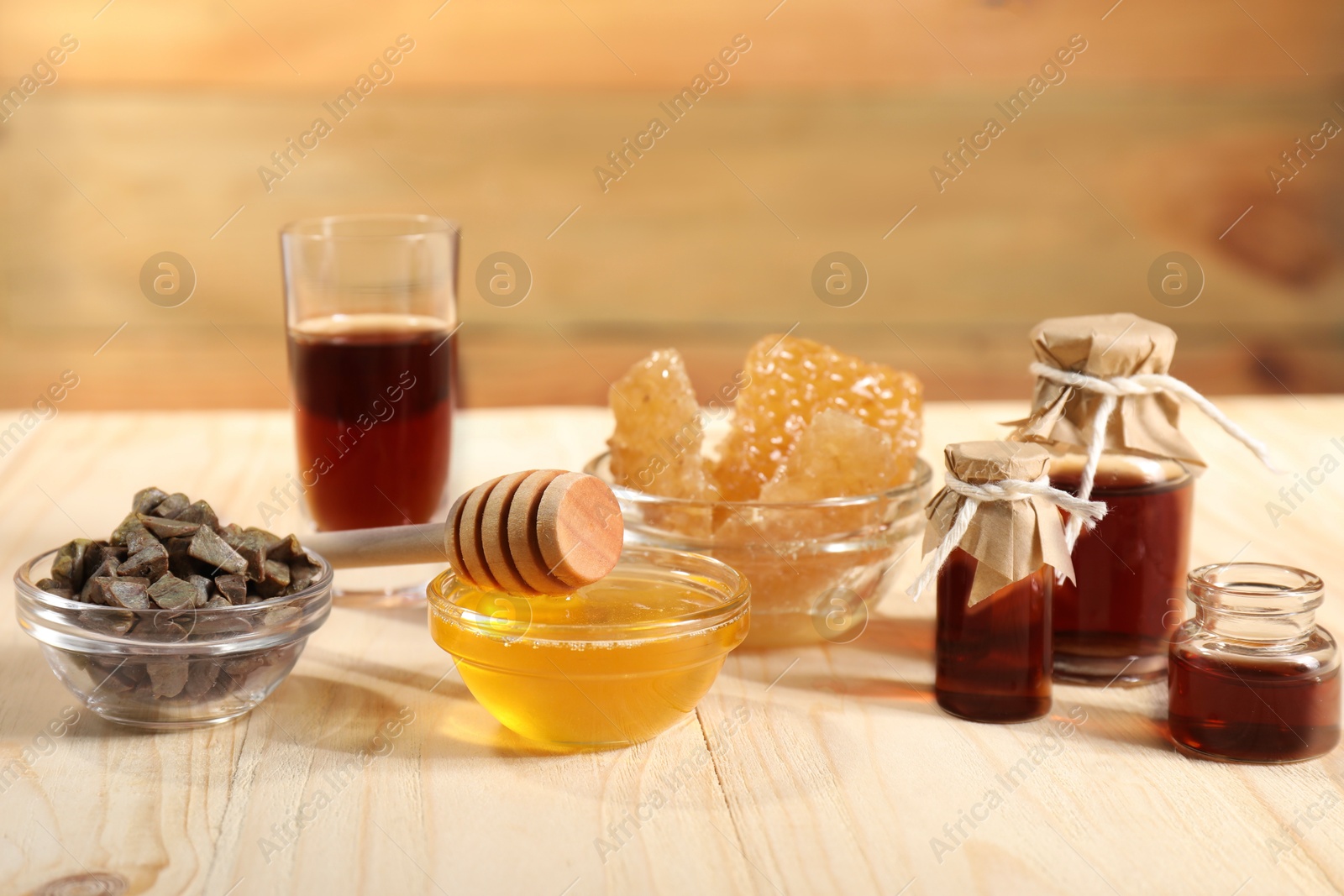 Photo of Honey, tincture, propolis granules and honeycombs on light wooden table, closeup. Alternative medicine