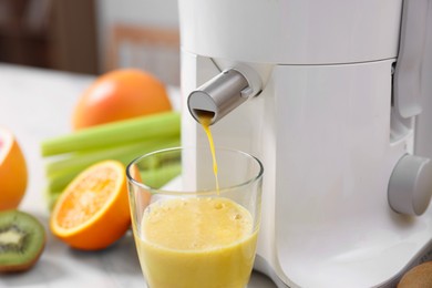 Photo of Modern juicer, glass and fresh fruits on table in kitchen, closeup