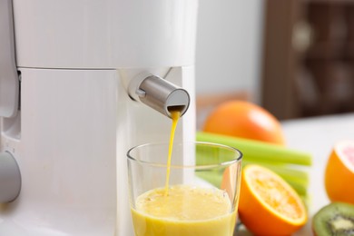 Photo of Modern juicer, glass and fresh fruits on table in kitchen, closeup