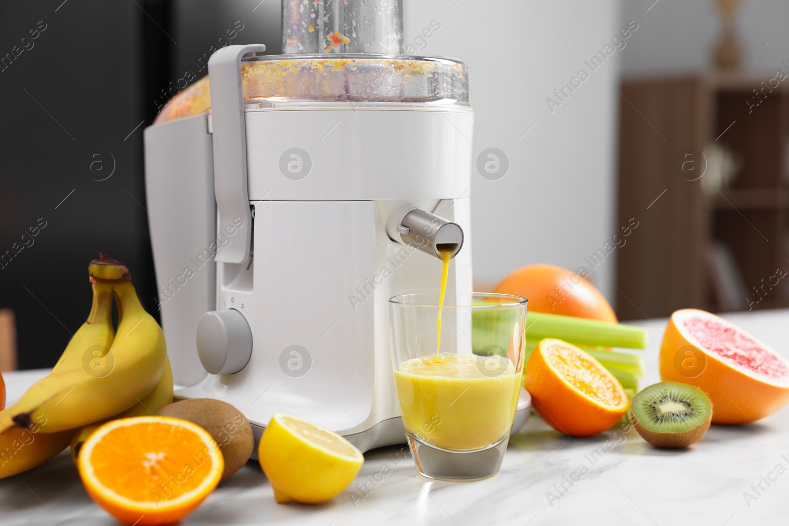 Photo of Modern juicer, fresh fruits and glass on white marble table in kitchen