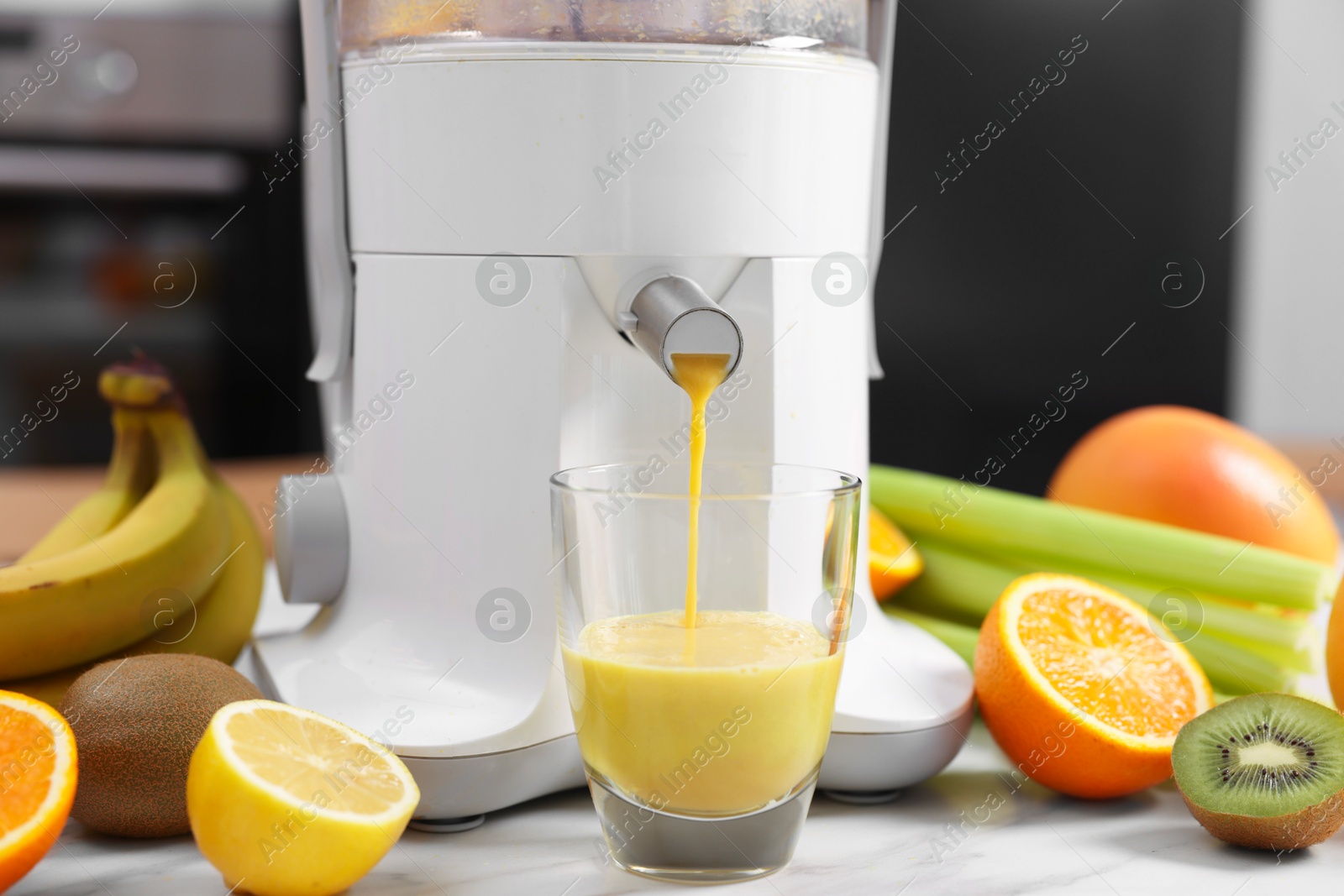 Photo of Modern juicer, fresh fruits and glass on white marble table in kitchen, closeup