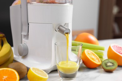 Photo of Modern juicer, fresh fruits and glass on white marble table in kitchen