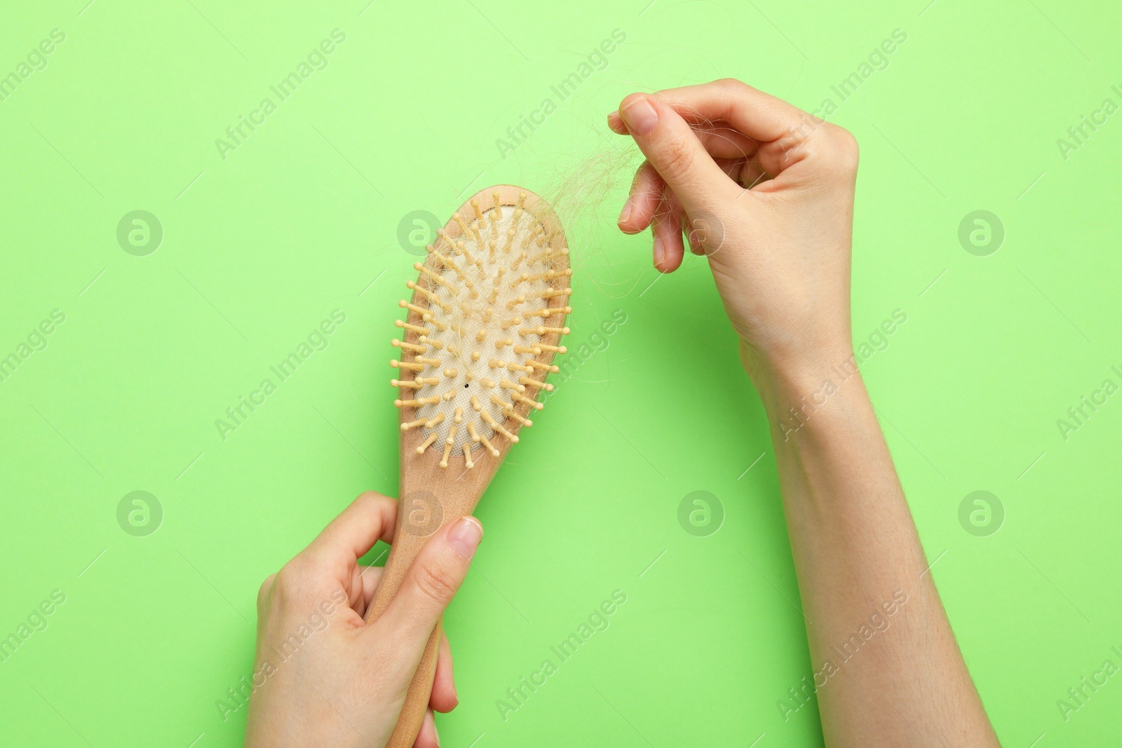 Photo of Woman taking her lost hair from brush on light green background, top view