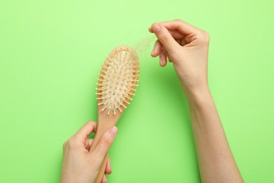 Photo of Woman taking her lost hair from brush on light green background, top view