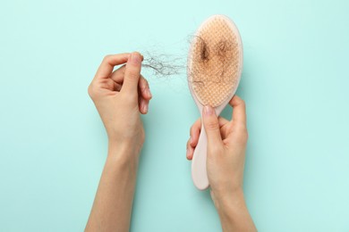 Photo of Woman taking her lost hair from brush on light blue background, top view. Alopecia problem