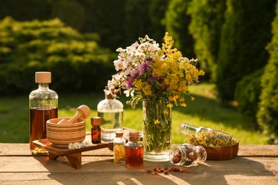 Photo of Different tinctures in bottles, ingredients, mortar and pestle on wooden table outdoors