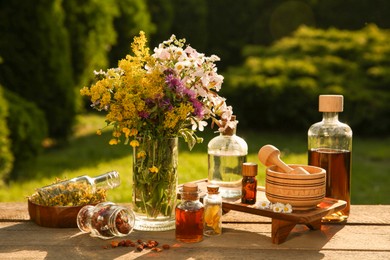 Photo of Different tinctures in bottles, ingredients, mortar and pestle on wooden table outdoors