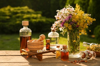 Photo of Different tinctures in bottles, ingredients, mortar and pestle on wooden table outdoors