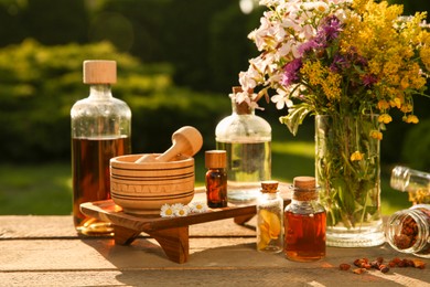 Different tinctures in bottles, ingredients, mortar and pestle on wooden table outdoors