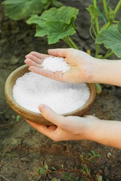 Woman holding plant fertilizer in bowl outdoors, closeup