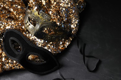 Beautiful carnival masks and fabric with golden sequins on black table, closeup