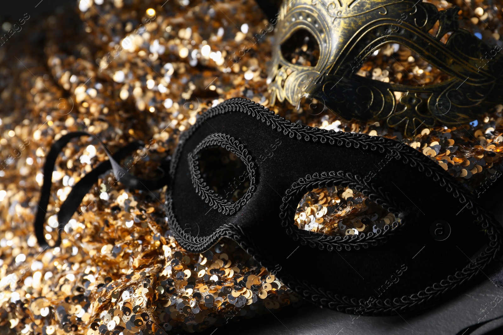 Photo of Beautiful carnival masks and fabric with golden sequins on black table, closeup