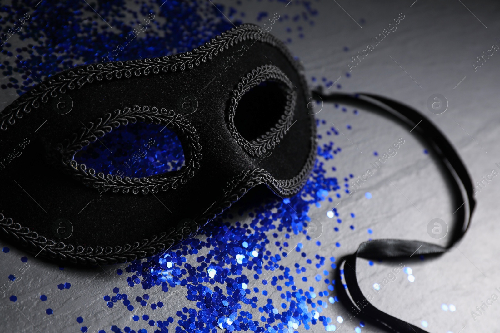 Photo of Beautiful carnival mask and blue sequins on black table, closeup