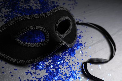 Photo of Beautiful carnival mask and blue sequins on black table, closeup