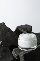 Photo of Face cream in jar on stones against light background