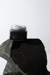 Face cream in jar on stone against light background