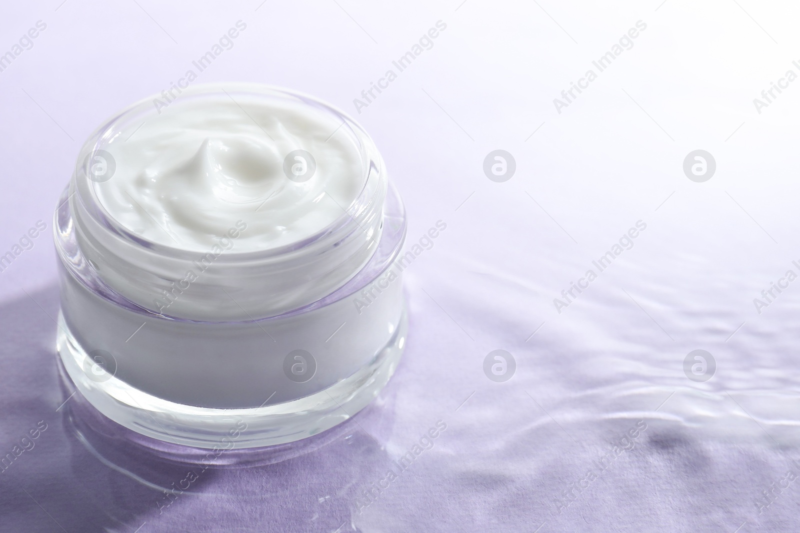 Photo of Jar with face cream in water on light violet background, space for text