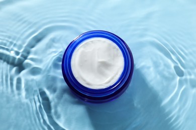 Jar with face cream in water on light blue background, top view