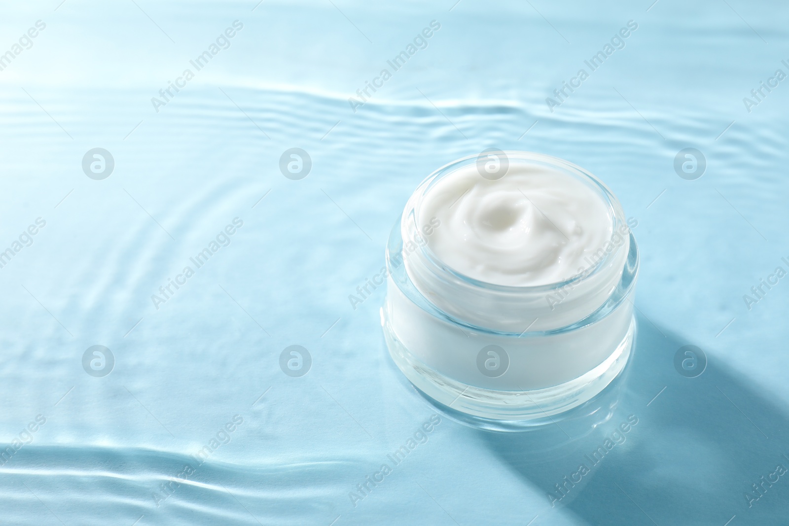 Photo of Jar with face cream in water on light blue background, space for text