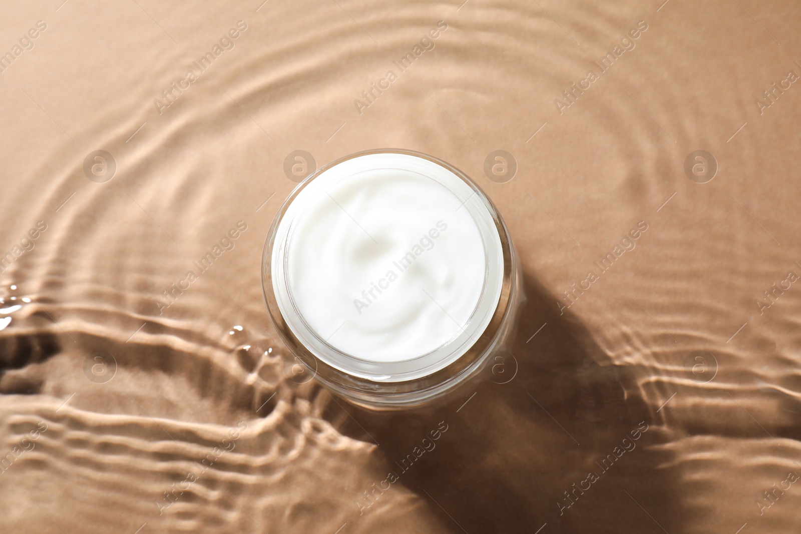 Photo of Jar with face cream in water on beige background, top view